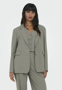 Šedý přílišný blazer s klopami, předními kapsami a zapínáním na knoflíky, doplněný odpovídající vestičkou. Hladká, strukturovaná tkanina.