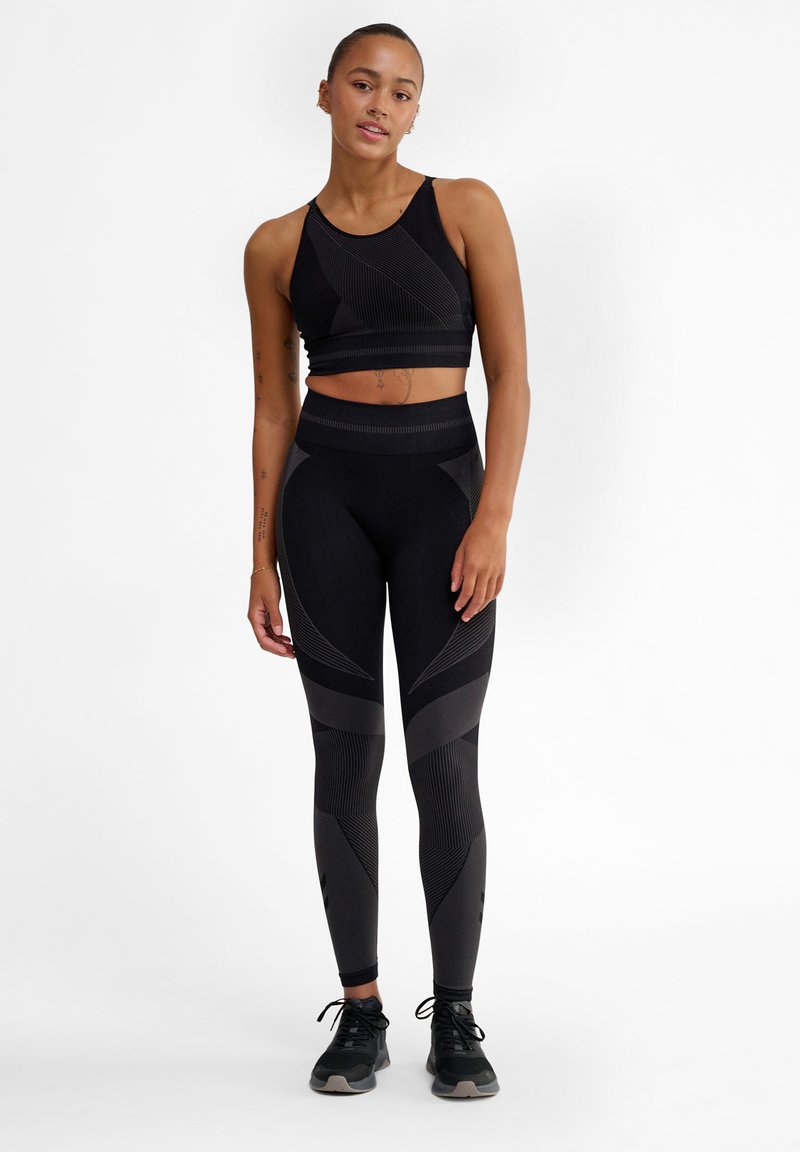 Svart träningsset bestående av en figurnära sport-bh med strukturerade ränder och högmidjade leggings med geometriska mönster.