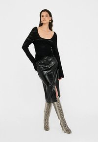 Top nero a maniche lunghe in maglia con scollo a U, abbinato a una gonna in pelle nera a vita alta con spacco laterale e stivali alti fino al ginocchio con motivo a fantasia.