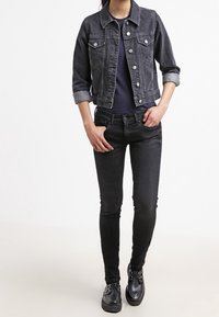 Czarna dżinsowa kurtka z podwiniętymi rękawami, w zestawieniu z dopasowaną czarną koszulą i czarnymi dżinsami. Footwear z siateczkowym wzorem z klamrami.
