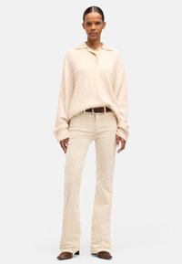 Beige oversized sweater med krave og knaplukning, kombineret med lyse beige udvidede bukser og mørkebrune ankelstøvler.