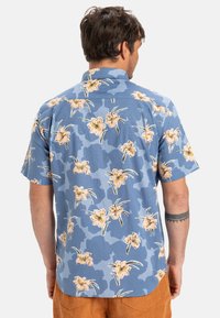 Korte mouwen, blauw, bloempatronen shirt met een camo-ontwerp, voorzien van roze bloemen en groene bladeren. Zachte stof en tail hem.