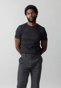 Czarna bawełniana koszulka z okrągłym dekoltem i krótkimi rękawami, zestawiona z ciemnoszarymi eleganckimi spodniami. Prosty design, minimalne akcenty.