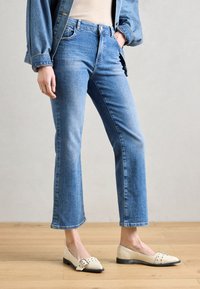 Blå denim jeans med en rett ben design, høy livhøyde, frontlommer, og et subtilt falmet mønster. Kombinert med kremfargede leiligheter med en stropp.