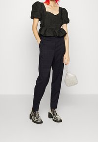 Svart texturerad peplumtop med puffärmar, i kombination med mörka rutiga byxor. Silverfärgade plattformsskor och en liten metallisk väska fullbordar looken.