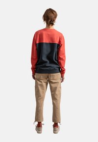 Felpa a maniche lunghe con parte superiore color corallo e sezione inferiore blu navy, abbinata a pantaloni cargo beige con tasche laterali e macchie di vernice visibili.