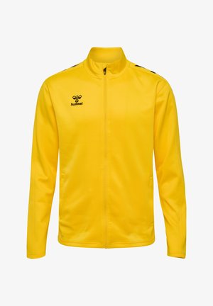 Gul sportjakke med høj krave, fuld lynlås, sidelommer og sort logo; lavet af glat, let vævning med en tætsiddende design.