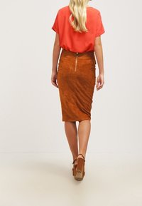 Brun mocka blyertskjol med en strukturerad yta, med en dragkedja i mitten bak och en lös röd blus med korta ärmar.