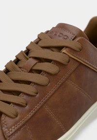 Baskets en cuir marron avec bout arrondi, semelle en caoutchouc beige, lacets texturés et détails de couture. Logo embossé sur la languette.