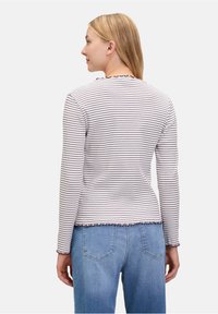 Gestreiftes Langarmshirt in Beige und Dunkelbraun, mit einem gewellten Ausschnitt und Saum, kombiniert mit hellblauen Jeans.