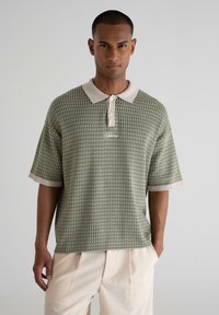Green patterned polo shirt with a beige collar and cuffs, featuring a textured weave and a single button placket.
