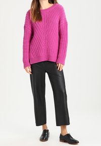 Rosa stickad tröja med ett kraftigt ribbmönster, ihop med svarta cropped byxor i faux läder och svarta snörskor.