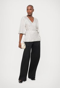 Top plateado con mangas acampanadas, combinado con pantalones negros de pierna ancha. El atuendo tiene una textura suave y una cintura ajustada con un lazo como detalle.