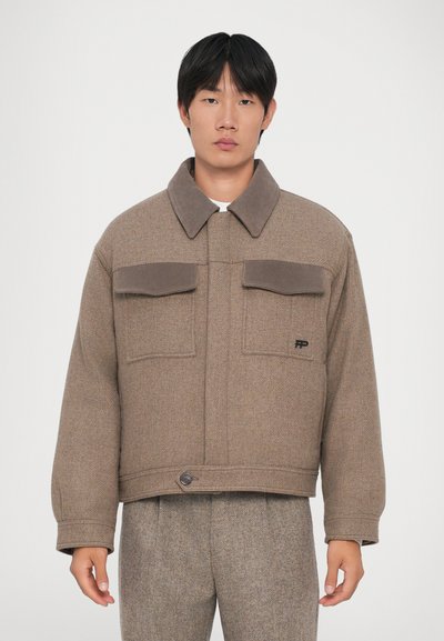 Veste courte à carreaux marron avec un col, deux poches avant et une fermeture à boutons. Texture douce avec des accents marron contrastants.