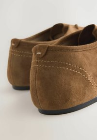 Mocassini in suede marrone con punta arrotondata, caratterizzati da cuciture a contrasto e una suola in gomma nera liscia; design minimalista senza elementi hardware.