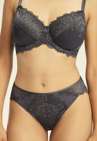 Dunkelgrauer Spitzen-BH mit floralem Muster und gewellten Kanten, kombiniert mit passenden hochgeschnittenen Slips, die ähnliche Details aufweisen.