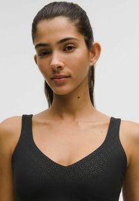 Sort ærmeløs top med V-hals-design, lavet af tekstureret materiale med et diskret prikket mønster. Nærbillede af halsudskæringen og skuldrene.