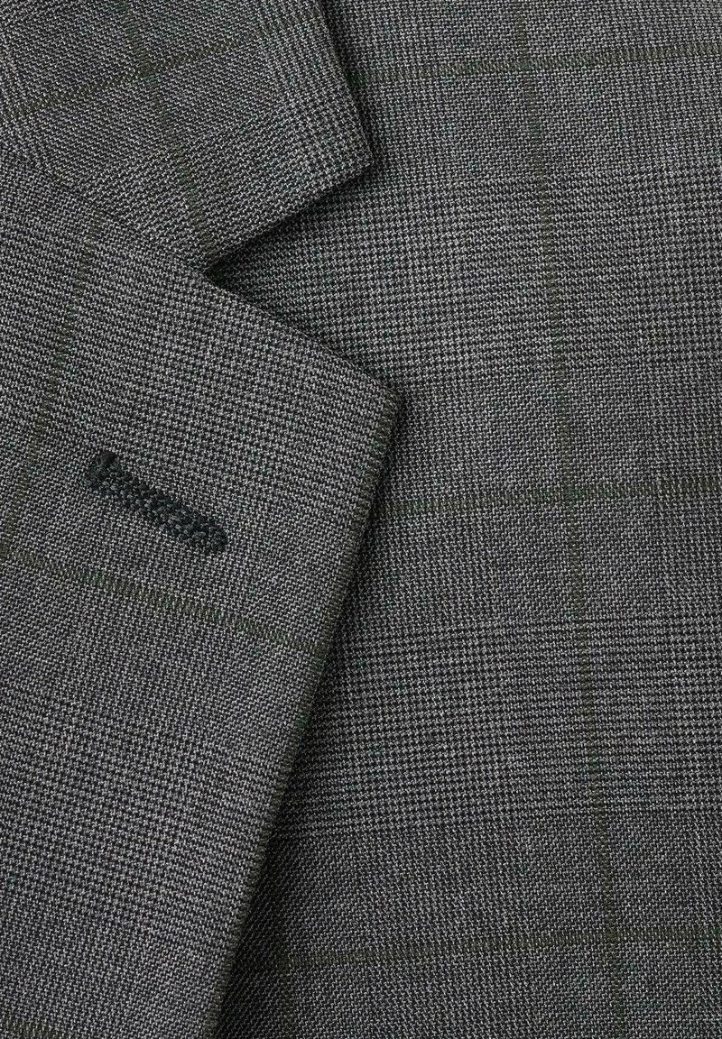 Grauer karierter Stoff mit kleinem Hahnentrittmuster, strukturierter Oberfläche und dezenten grünen Akzenten auf überlappenden Blazer-Revers.
