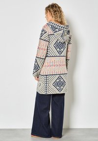 Sweter z kapturem z geometrycznymi wzorami w granatowym i jasnobeżowym kolorze, z różowymi akcentami. Krój jest luźny z prostym dołem.
