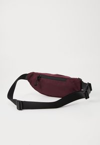Ceinture banane bordeaux avec une fermeture éclair noire, une sangle réglable et une texture de tissu lisse. Elle dispose d'une petite poche avant pour le rangement.
