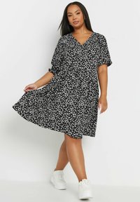 Musta kukallinen mekko, jossa on V-pääntie, lyhyet hihat ja rypistetty vyötärö. Mekossa on valkoisia kukkakuoseja ja laskostettu helma. Yhdistetty valkoisiin lenkkareihin.