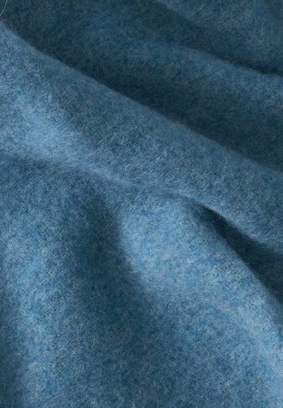 Tissu bleu doux avec une texture duveteuse, montré en gros plan avec des plis délicats et des ombres mettant en valeur son matériau.