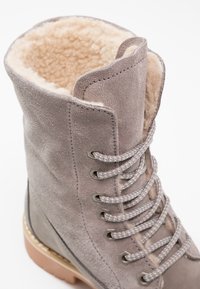 Stivaletto in suede grigio con fodera in finta pelliccia, punta tonda e occhielli metallici. Presenta lacci texture e una suola robusta di colore chiaro.