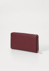 Burgundská kožená peněženka s elegantním obdélníkovým designem. Disponuje zlatým zipem a malou kovovou nášivkou na poutku zipu.