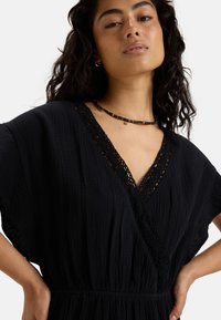 Black dress featuring a V-neck and short sleeves with lace detailing, soft textured fabric, and an elastic waist for a relaxed fit.