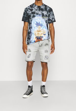 Koszulka graficzna w czarnym tie-dye z kolorowym nadrukiem "Dragon Ball Super"; jasnoszare spodenki z efektem postarzania w wzór zebry; czarne wysokie sneakersy.