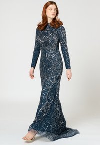 Robe de soirée en sequins bleu marine avec manches longues, motifs en tourbillon complexes et ourlet légèrement évasé, associée à des sandales à talons hauts.