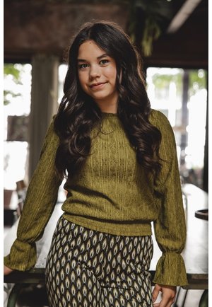 Olijfgroen, gestructureerd sweater met uitlopende mouwen, gecombineerd met zwart-witte, gestreepte wijde broek met een oogmotief.