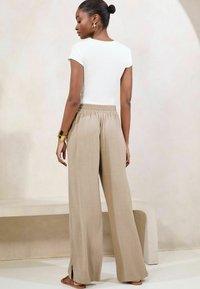 T-shirt bianco attillato e pantaloni beige a gamba larga con spacchi laterali. Tessuto morbido, vestibilità rilassata e vita elasticizzata. Accessorio con bracciale dorato.