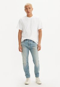Camiseta blanca de algodón de manga corta combinada con jeans de un azul claro y zapatillas blancas. La camiseta tiene un escote redondo y un corte relajado.