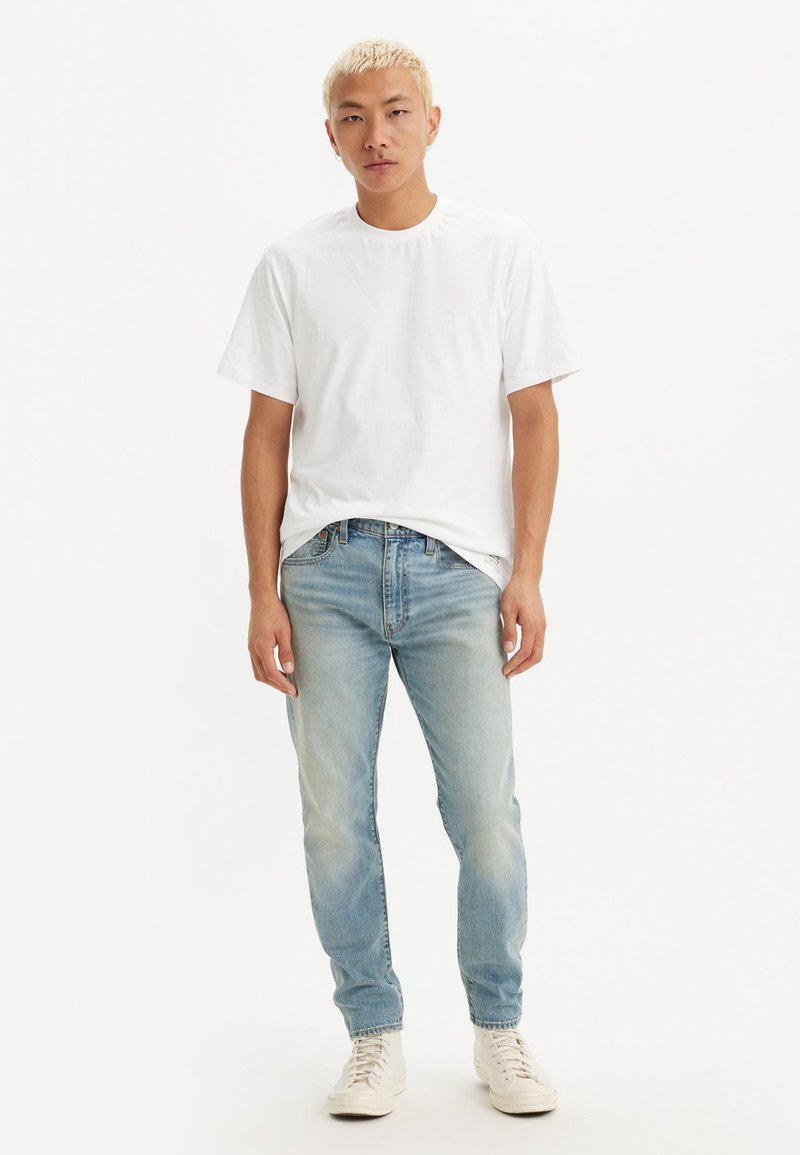 Camiseta blanca de algodón de manga corta combinada con jeans de un azul claro y zapatillas blancas. La camiseta tiene un escote redondo y un corte relajado.