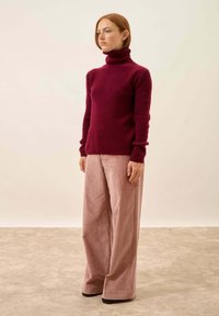 Burgundowy sweter z ryżowym splotem i golfem w połączeniu z jasnoróżowymi, szerokimi spodniami z kordurowej tkaniny. Gładka tekstura z dopasowanymi rękawami, czarne buty.
