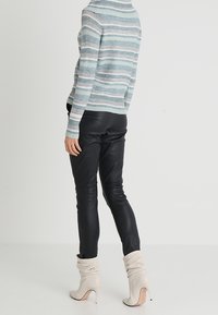 Pull rayé bleu clair et gris à col montant, associé à un pantalon en cuir noir et des bottines à talons souples de couleur crème.