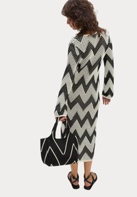 Abito lavorato a maglia con motivo zigzag in bianco e nero, maniche lunghe, abbinato a una borsa a righe in bianco e nero e sandali neri piatti.