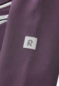 Lila tyg med en slät yta, prydd med en silverlogotyp i fyrkantig form och en silverdragkedjedetalj.