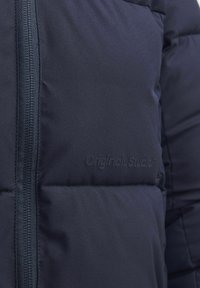 Marineblå jakke med fyld, quiltet design, lynlås i front og diskret branding. Glat tekstur og isoleret for varme.