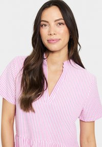 Robe rayée rose et blanche avec un décolleté en V, des manches courtes et une jupe froncée. Tissu léger avec une texture lisse.