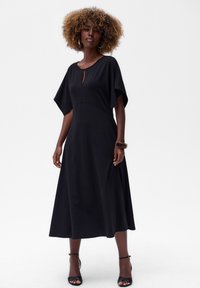 Schwarzes, mittel-lang Kleid mit kurzen, weiten Ärmeln und einem Schlüsselloch-Ausschnitt am Kragen; weicher Stoff, fließende Form und minimalistisches Design.