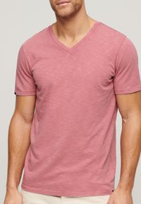 Rosa bomullsv-neck t-shirt med korta ärmar, något texturerad tyg och en neutral bakgrund. Minimalistisk design utan synliga mönster.