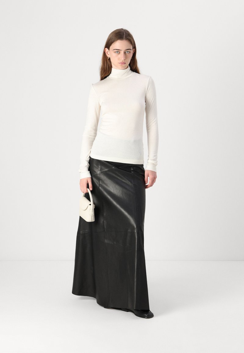 Witte coltrui gecombineerd met een lange zwarte leren rok. De outfit heeft een gestructureerde afwerking en een kleine crèmekleurige handtas.