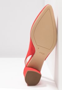 Chaussure à talon haut en daim rouge à bout pointu, présentée avec la semelle visible, sur un fond blanc en angle, avec le nom de la marque "högl" visible sur la semelle.