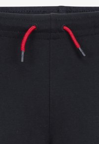 Calças de treino pretas com uma cintura preta e cordões de ajuste vermelhos, textura suave e costura reforçada. Inclui material de ajuste nas pontas.