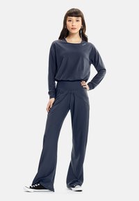 Dark gray, long-sleeve top with a wide neckline paired with matching, loose-fit pants featuring a high waistband and smooth texture. Black sneakers.
