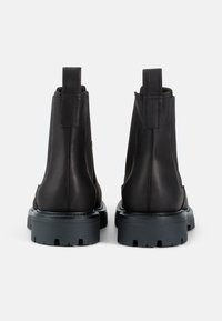 Botas de tobillo de cuero negro con tiradores, paneles laterales texturizados y suelas de goma gruesas con surcos profundos para una mejor tracción.