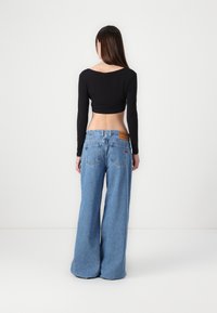 Musta lyhythihainen crop-top, joka on yhdistetty leveälahkeisiin sinisiin farkkuihin. Farkuissa on takana paikka ja kaksi takataskua.