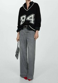 Pull noir en maille oversize avec un contour blanc et un motif "84", associé à un jean gris taille haute à jambes larges et des talons rouges.